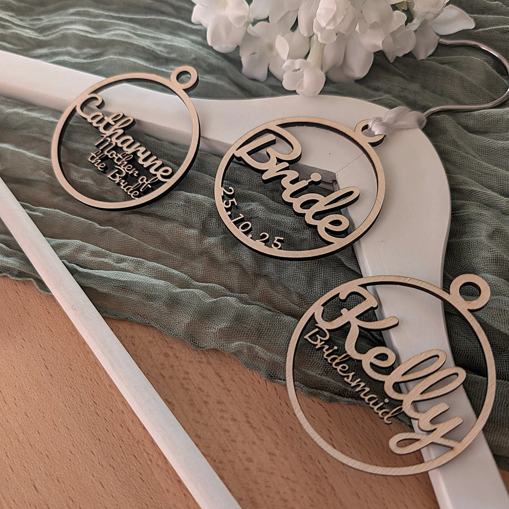 Three personalized hanger tags for a bride and her bridesmaids on a fabric background.