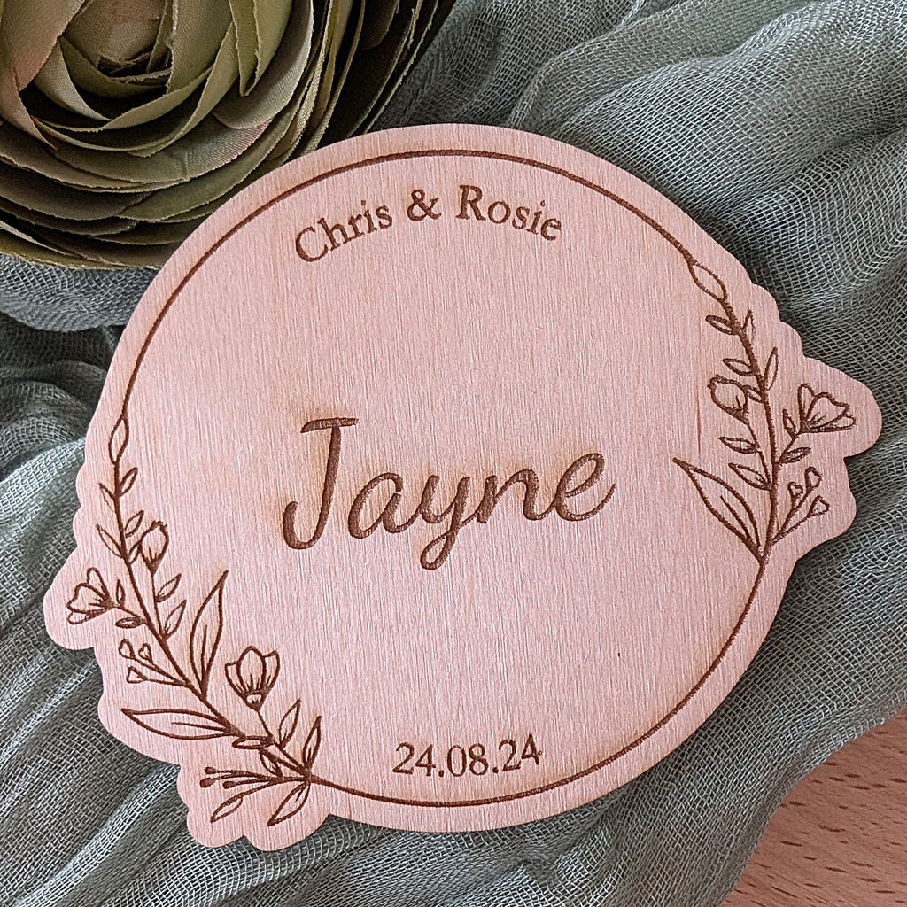 Wooden nameplate with engraved text 'Chris & Rosie Jayne 24.08.24' on a textured fabric background