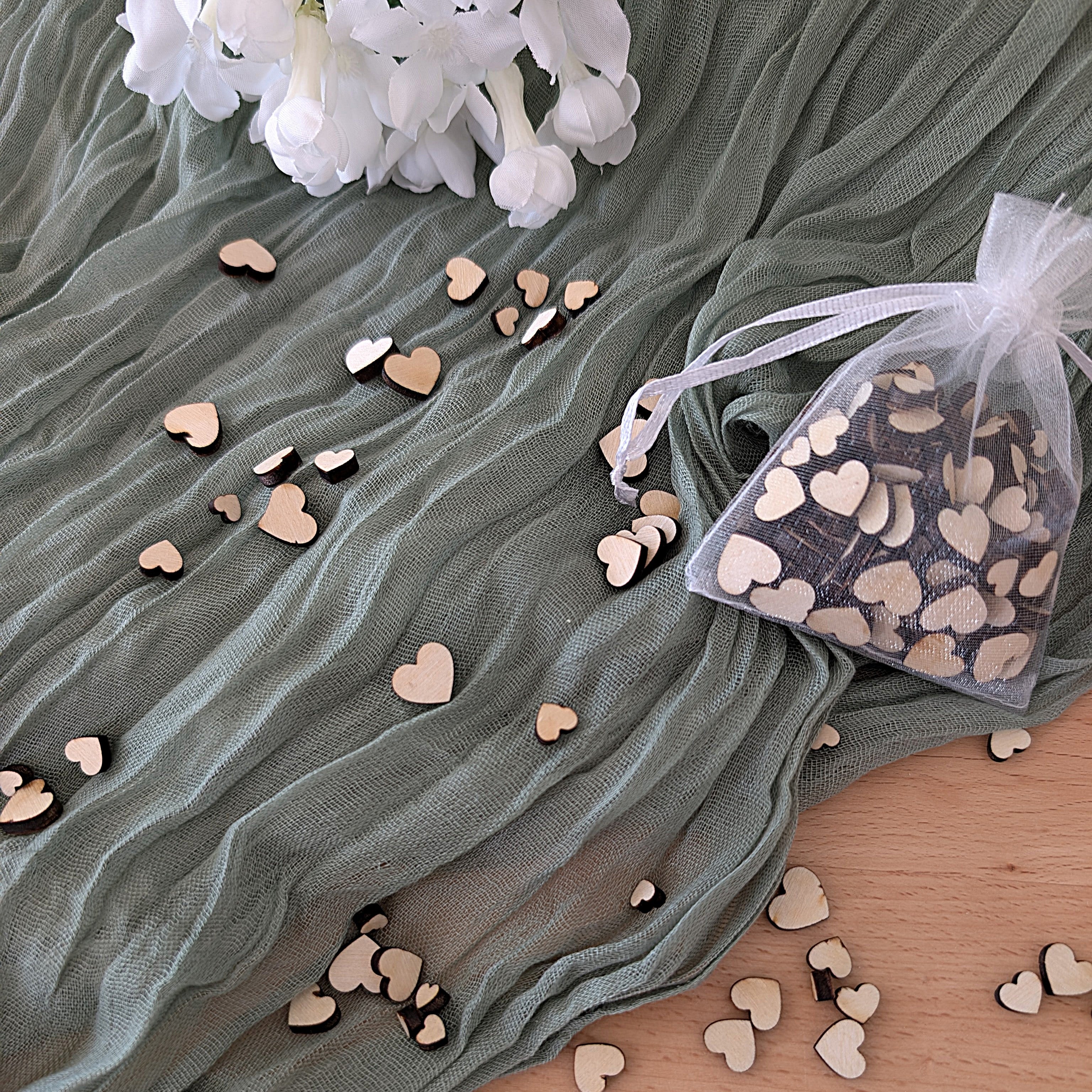 Wooden heart-shaped confetti on a textured fabric surface with a bag of confetti.