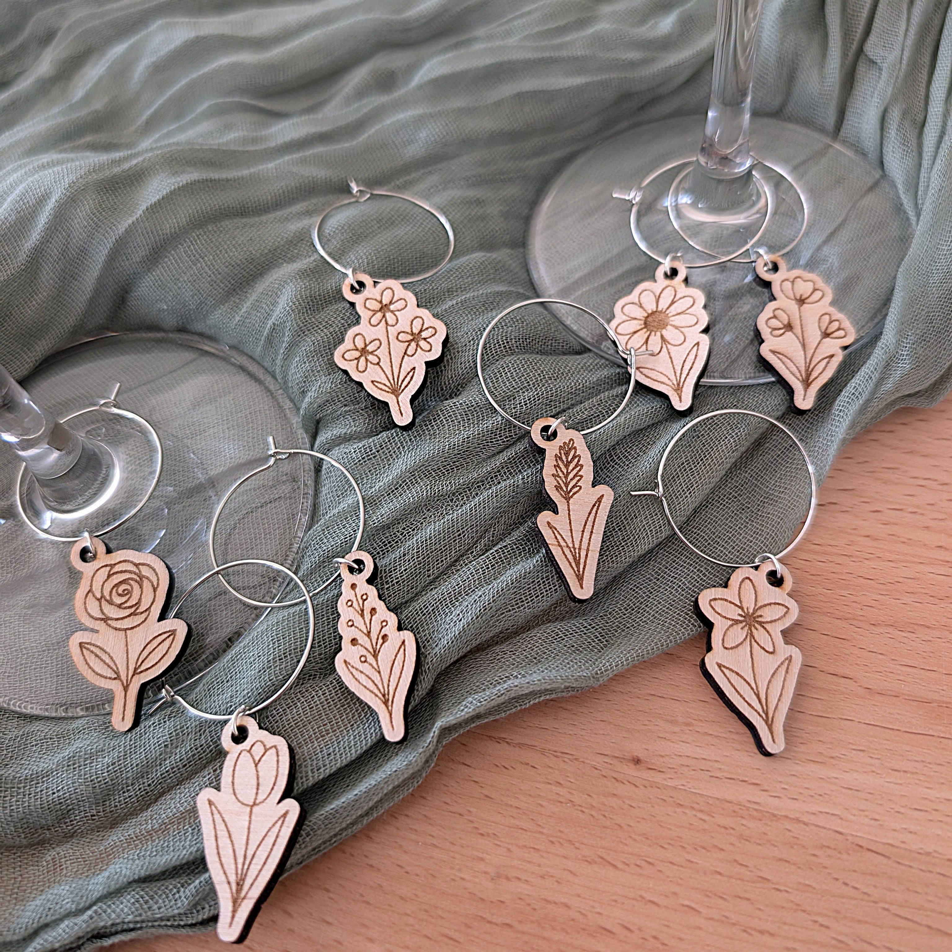 Decorative wine glass charms with floral designs on a green fabric background