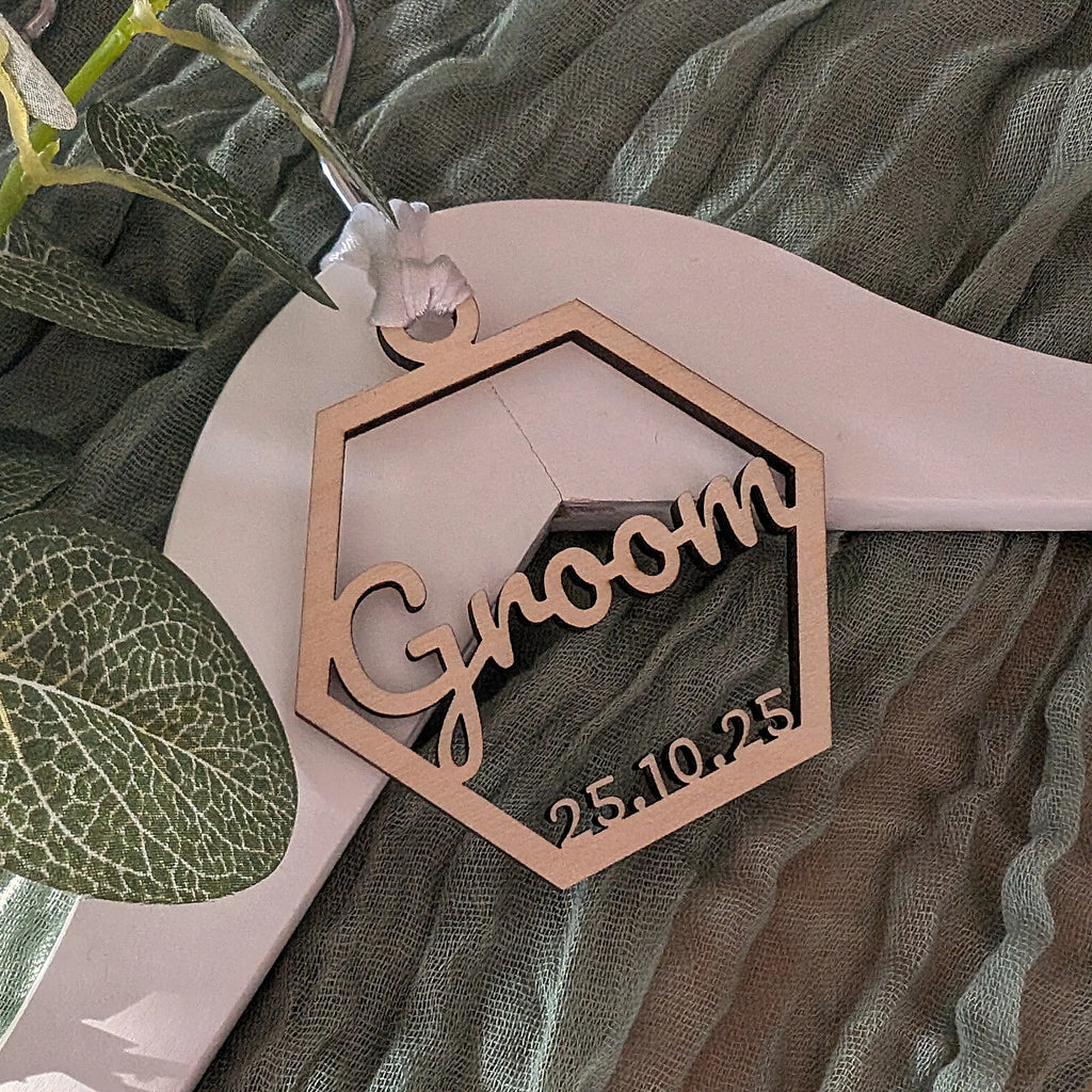 Wooden 'Groom' sign with date on a hanger against a green fabric background