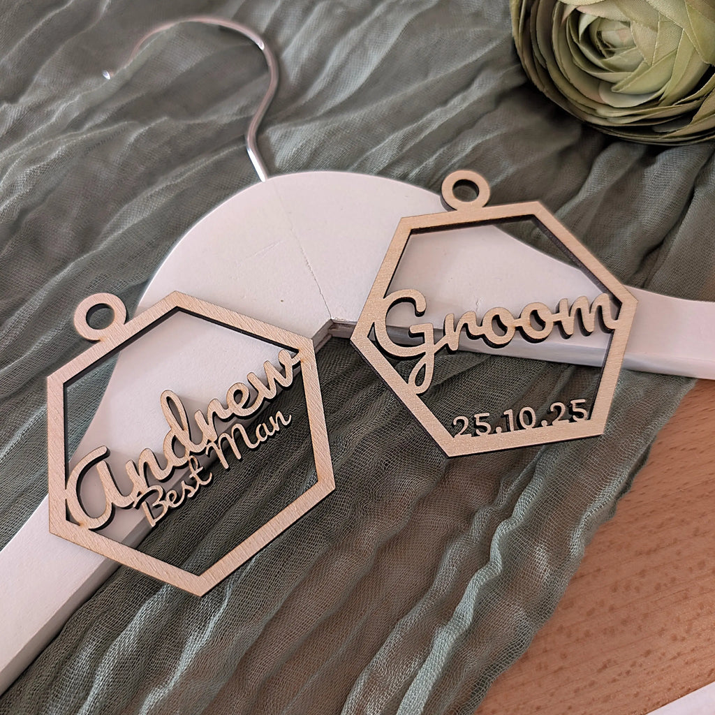 Personalized wooden name tags for a wedding, one labeled 'Andrew Best Man' and the other 'Groom', on a white hanger.