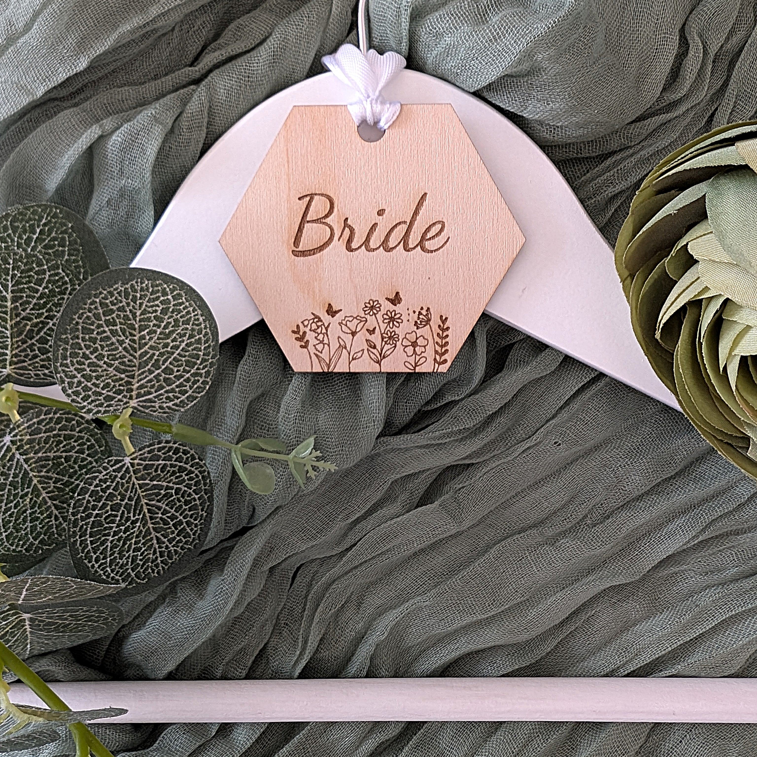 Wooden hexagonal tag labeled 'Bride' on a green fabric background with floral elements.