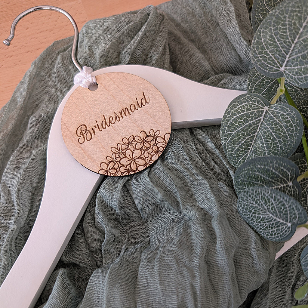 White hanger with wooden 'Bridesmaid' tag on a green fabric background