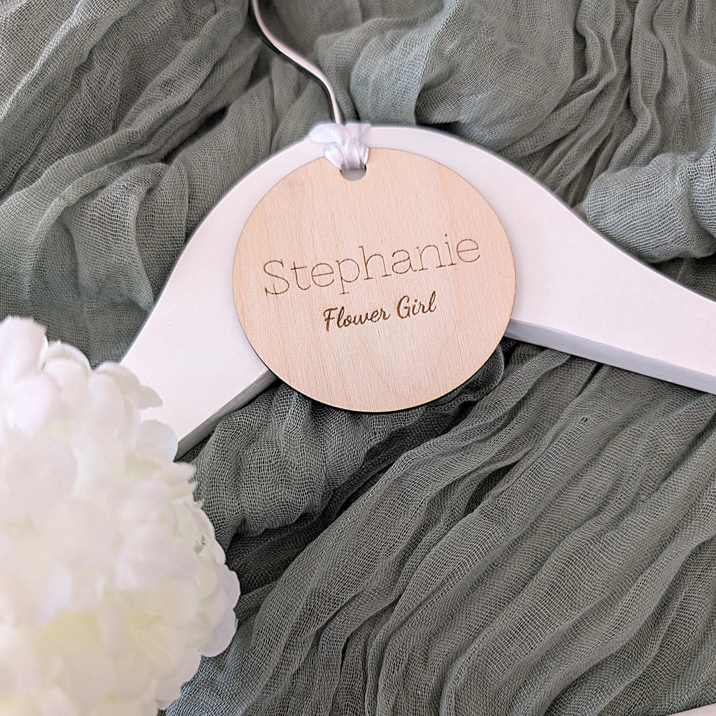 Wooden tag with 'Stephanie Flower Girl' on a white hanger with green fabric background