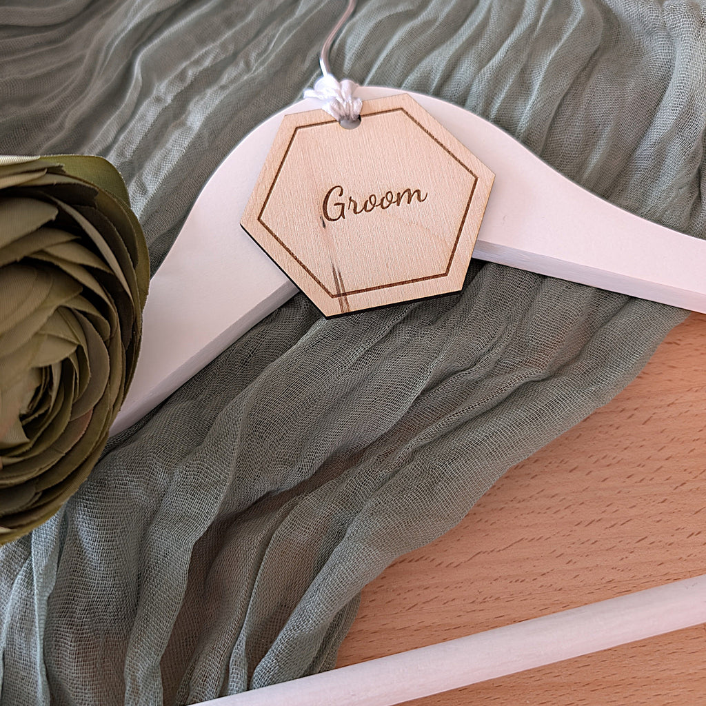 Wooden hanger with 'Groom' tag on a fabric background