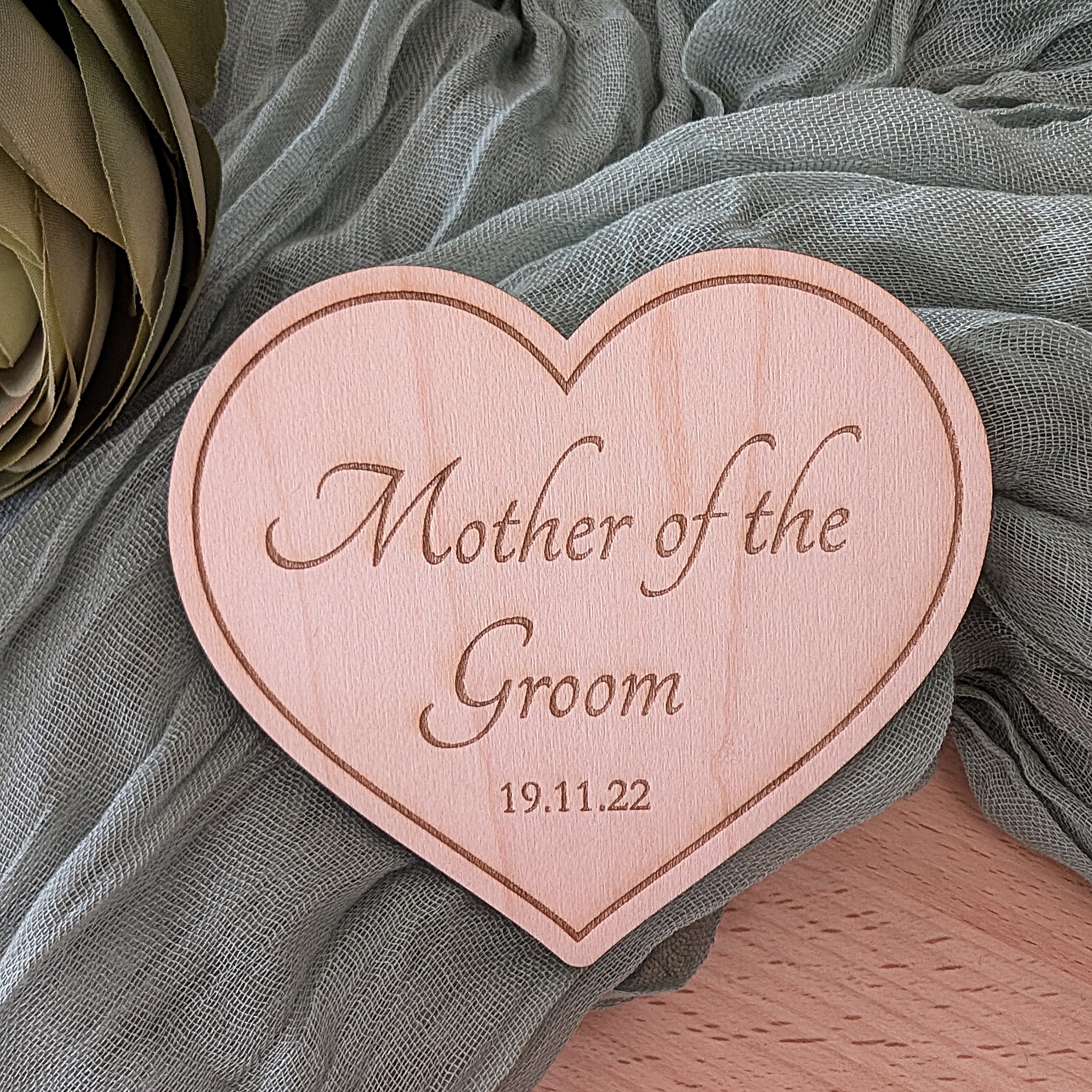 Heart-shaped wooden plaque with 'Mother of the Groom' and date engraved on a green fabric background