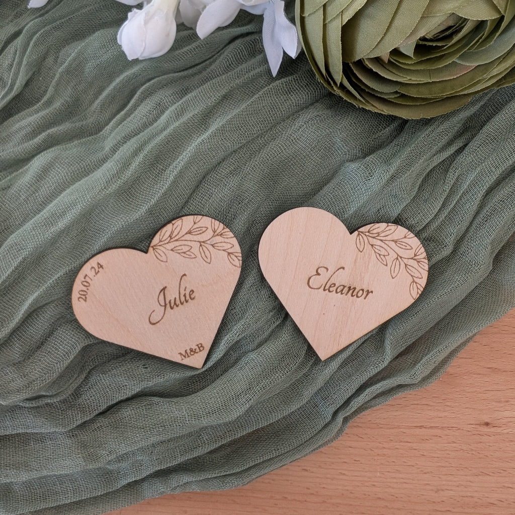 Two heart-shaped wooden name tags with engraved names on a green fabric background.