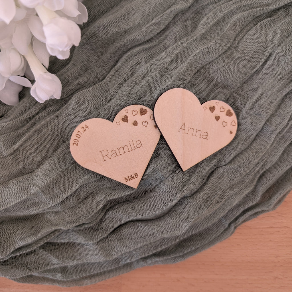 Two heart-shaped wooden nameplates with engraved names on a textured green fabric background.