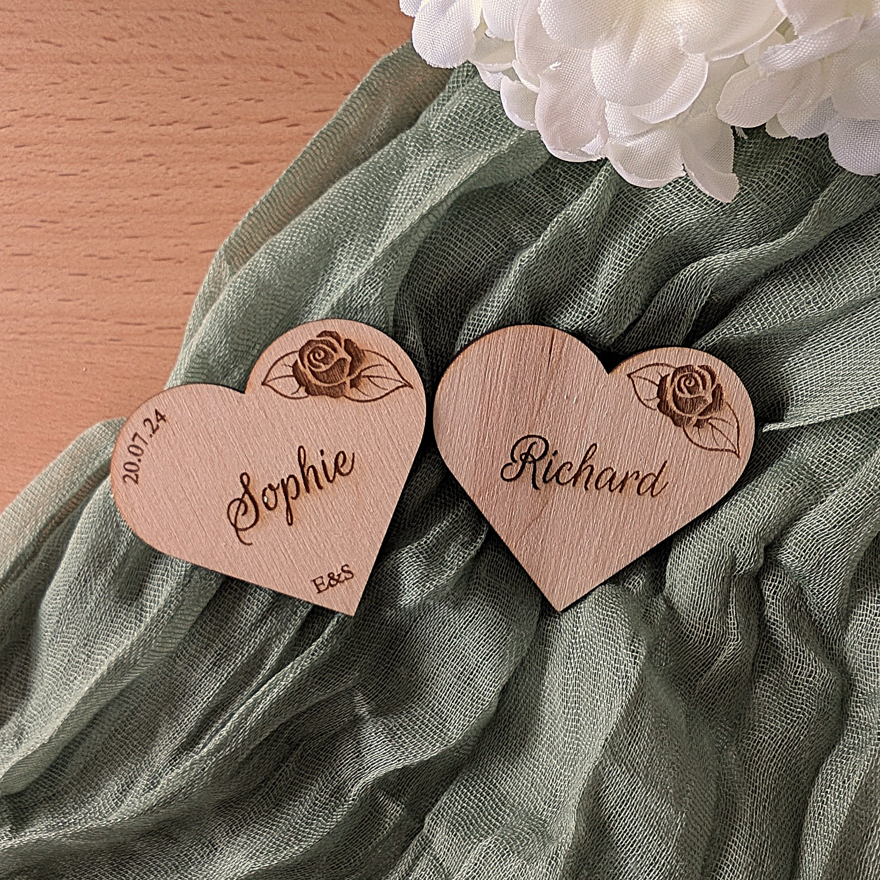Two wooden heart-shaped name tags with engraved names on a green fabric background.