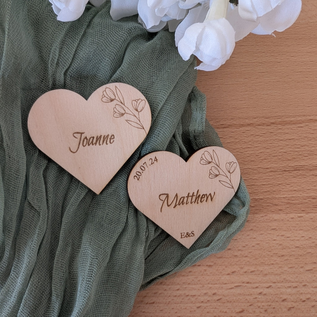 Heart-shaped wooden nameplates with engraved names on a green fabric background.