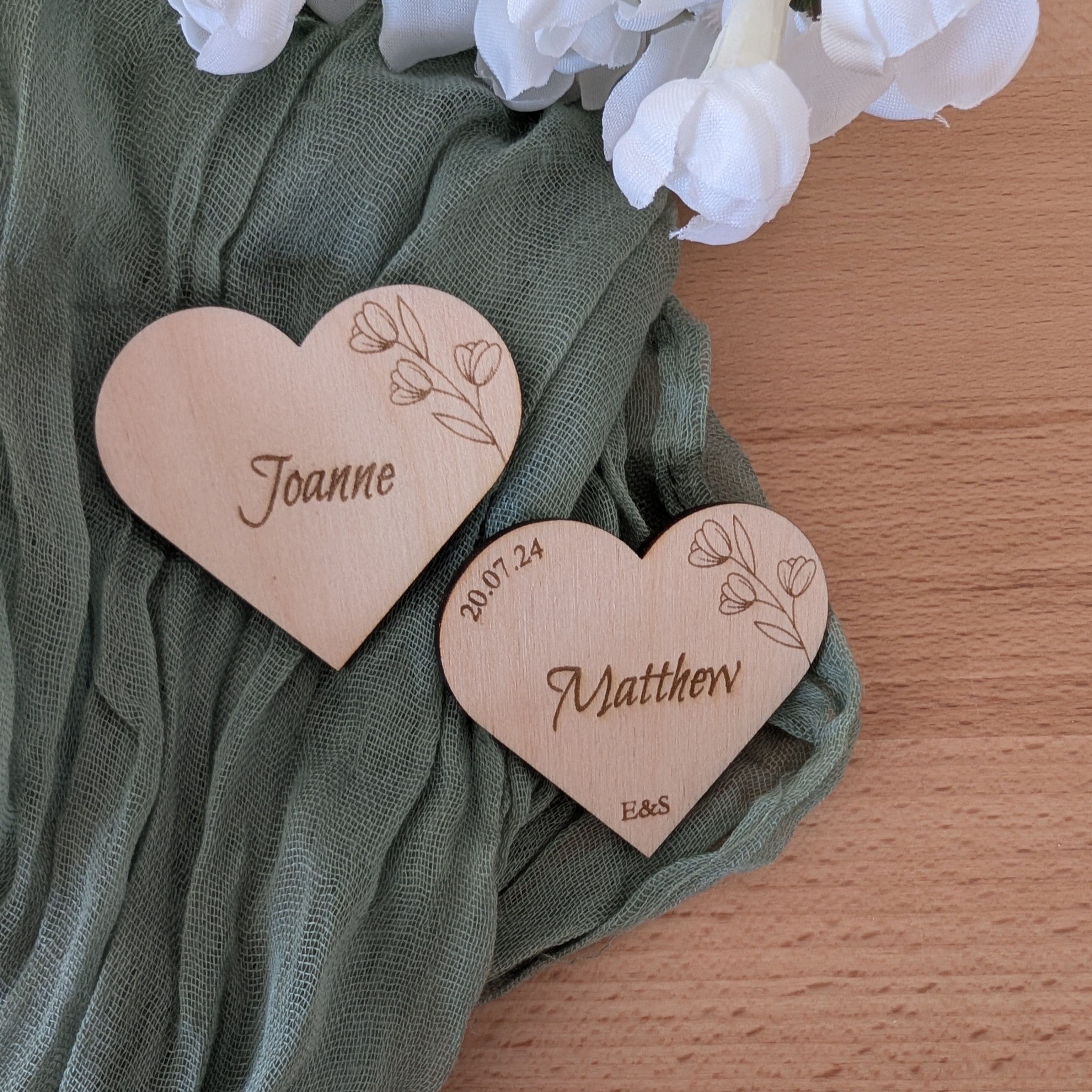 Heart-shaped wooden nameplates with engraved names on a green fabric background.