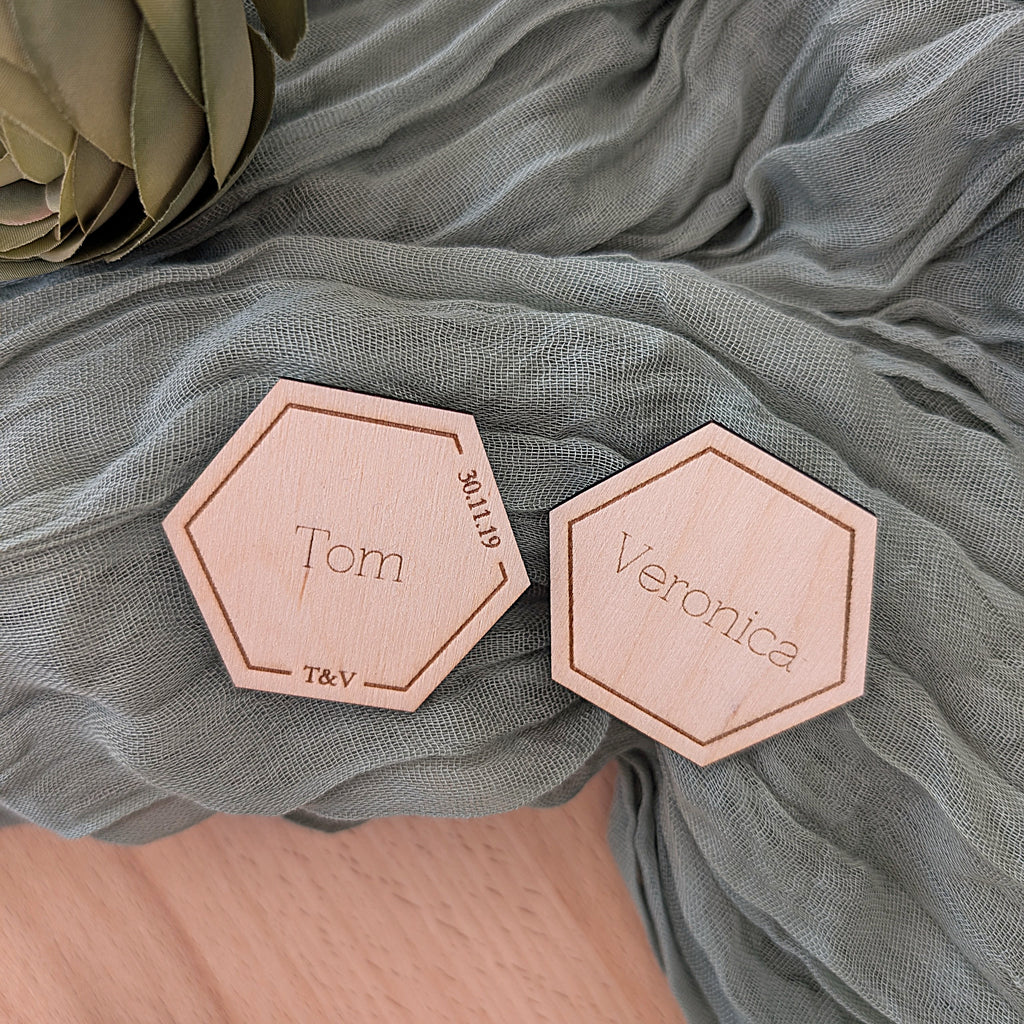 Hexagonal wooden nameplates with 'Tom' and 'Veronica' on a soft green fabric background