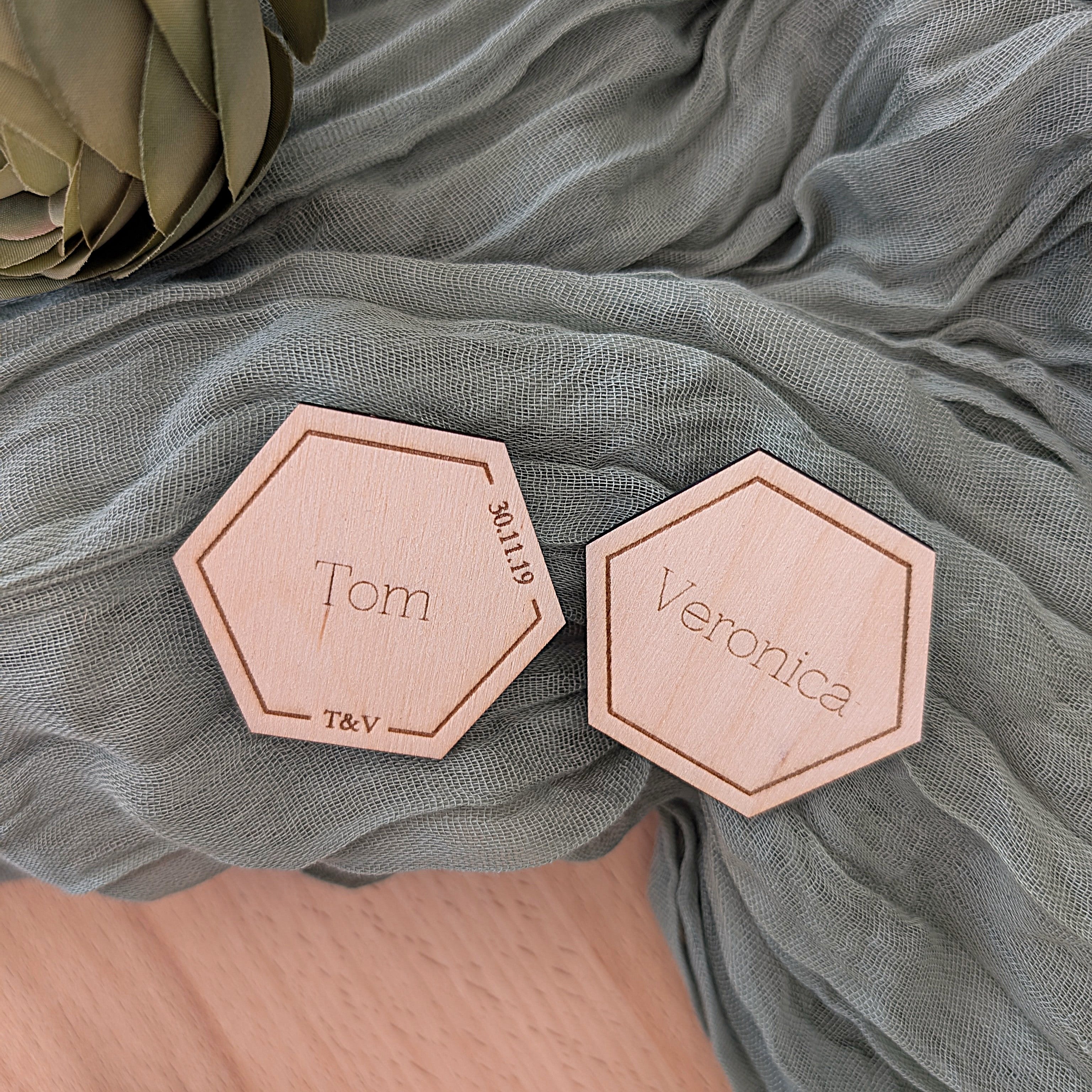 Hexagonal wooden nameplates with 'Tom' and 'Veronica' on a soft green fabric background