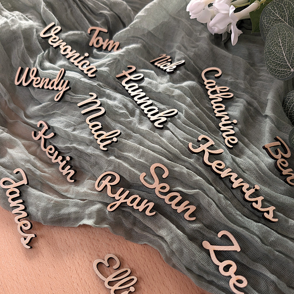 Wooden nameplaques on a textured fabric background with flowers and leaves.