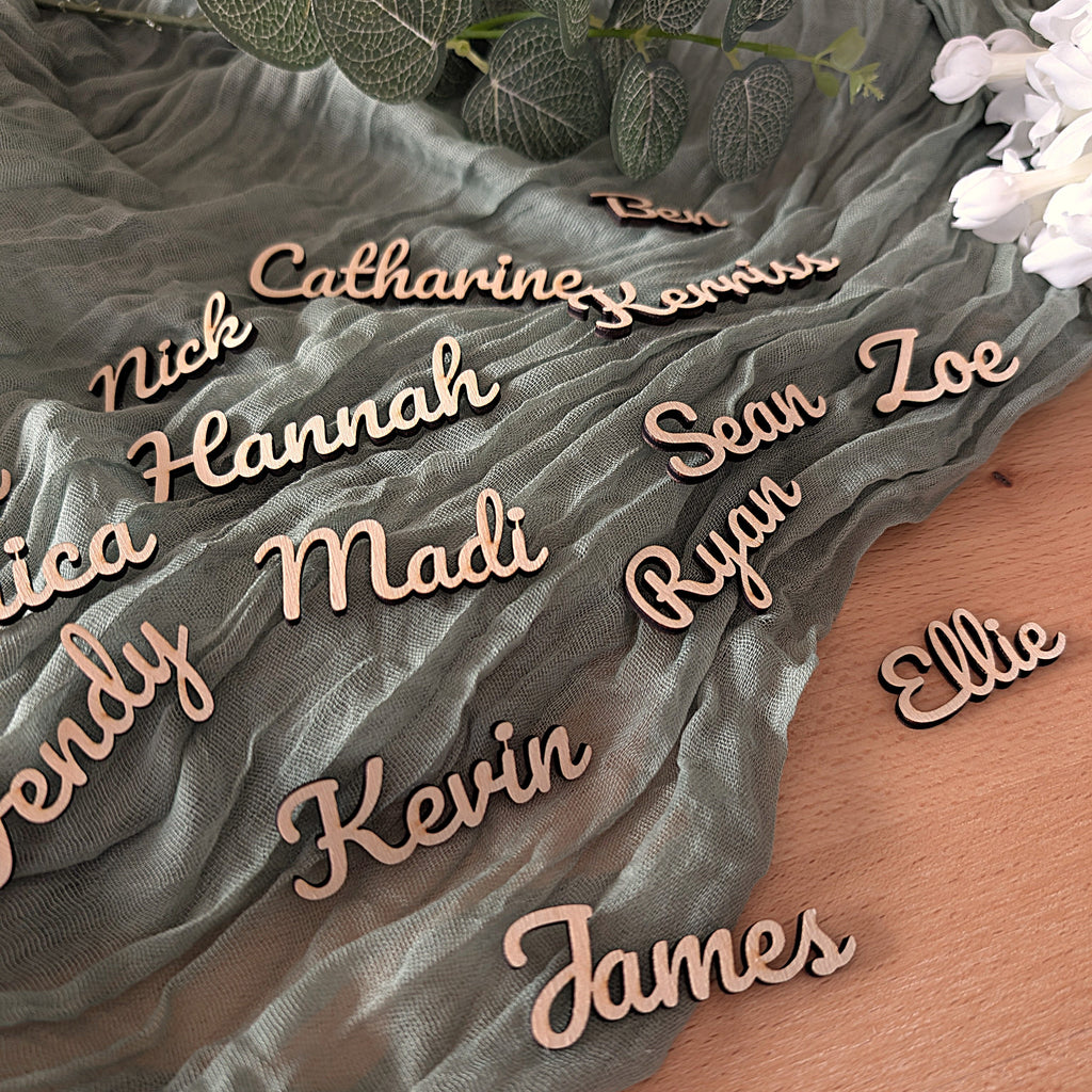 Wooden name placards on a textured fabric surface with flowers and leaves.