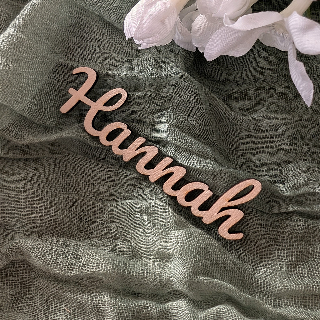 Wooden name 'Hannah' on a textured fabric background with white flowers.