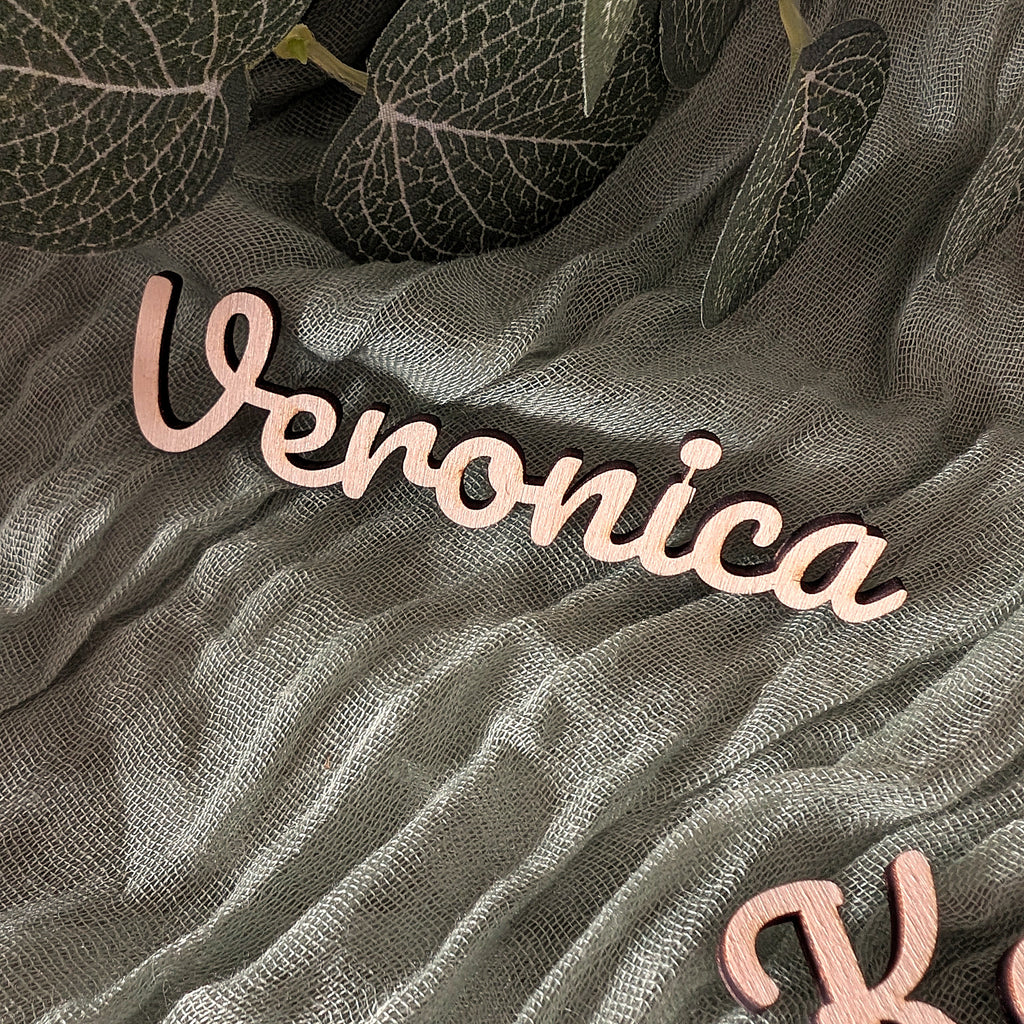 Wooden name 'Veronica' on a textured fabric background with leaves.