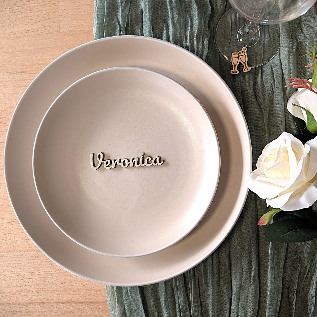 Beige ceramic plate with 'Veronica' engraving on a wooden surface with green fabric and flowers.